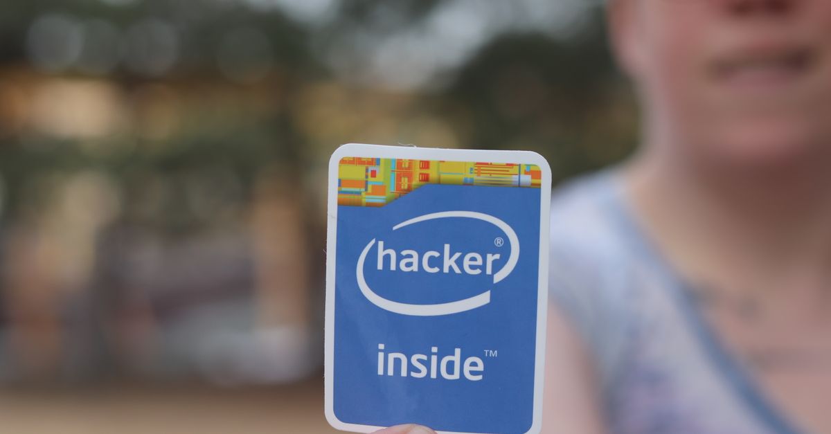 Person holding a 'hacker inside' sticker in an outdoor setting with blurred background.